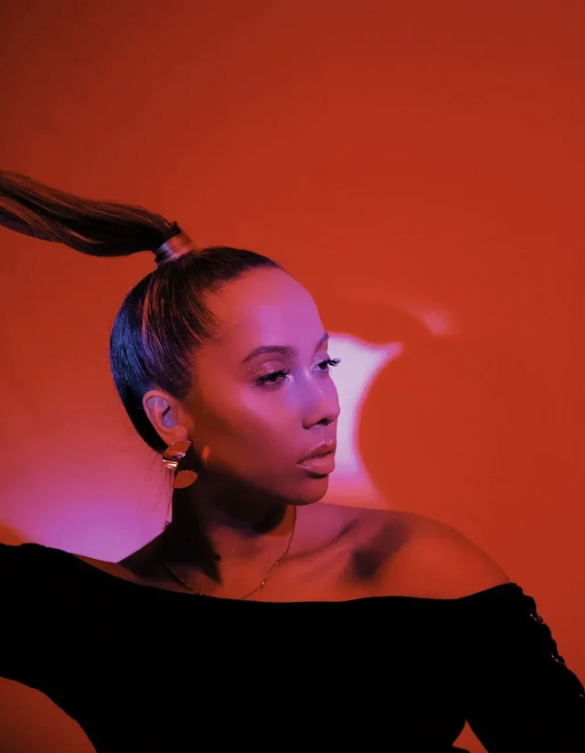 ROMII in profile against a red wall, hair in a high ponytail