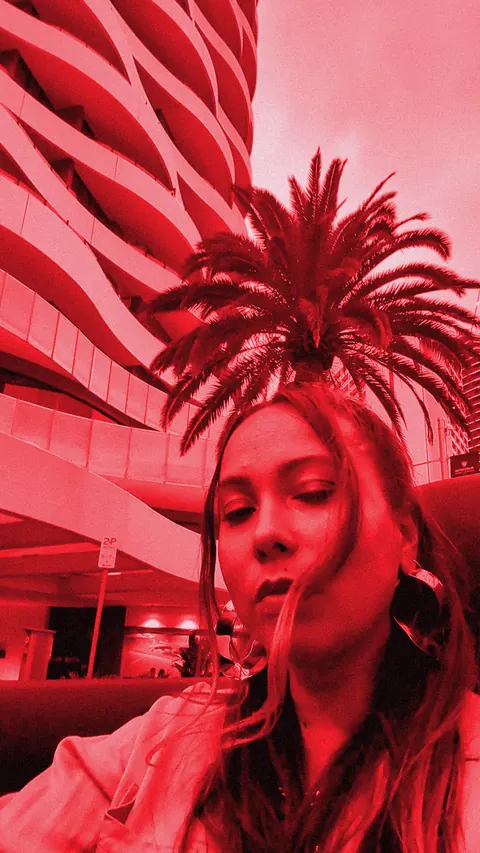 ROMII in a convertible under a palm tree and a curved Surfers Paradise tower, red-toned still