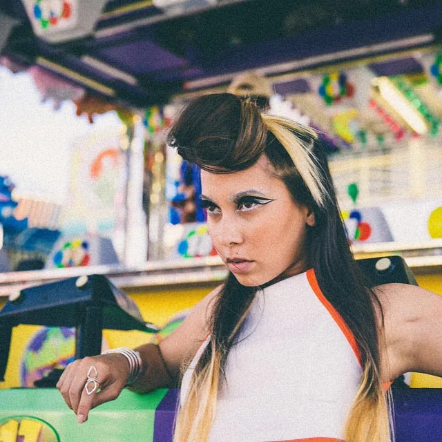 ROMII with sculpted hair and graphic eyeliner at a carnival stall