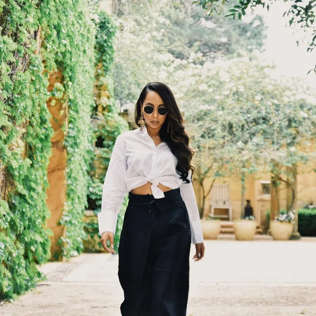 ROMII walking through a garden in a white shirt and round sunglasses