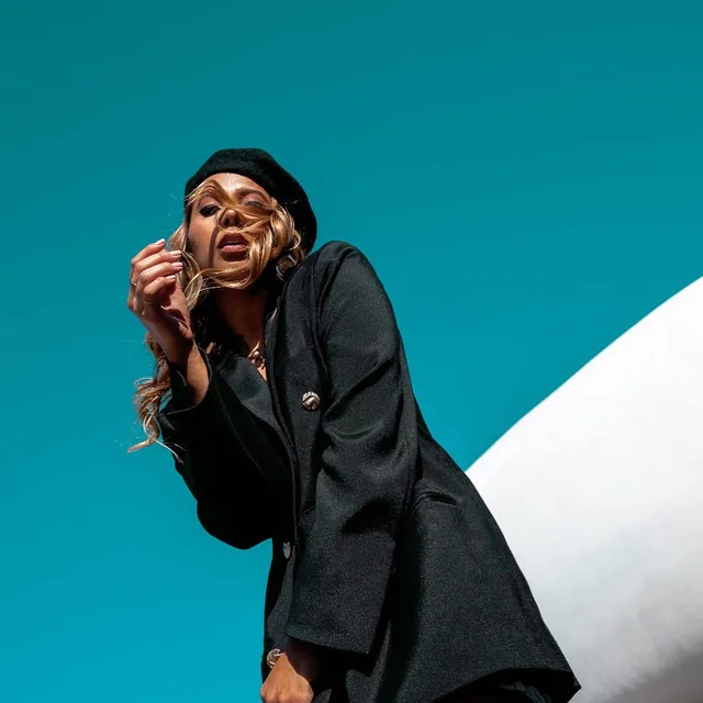 ROMII in a black beret and blazer against a teal sky